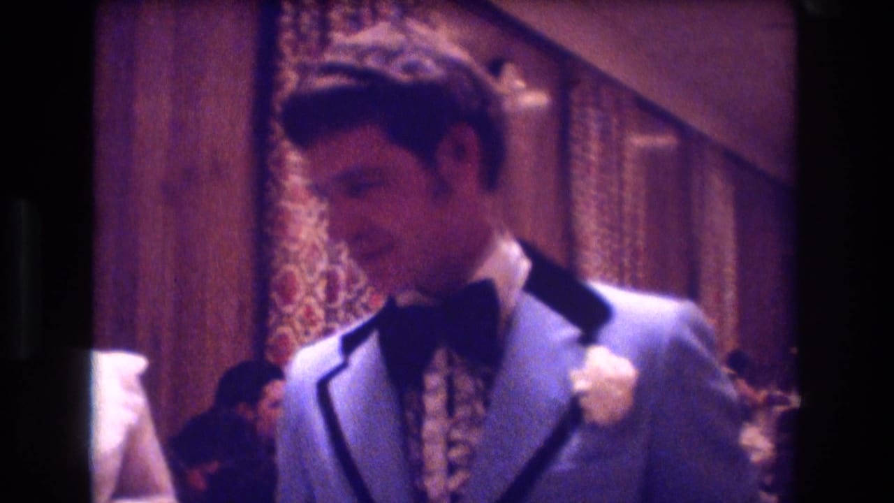 A young man in a light blue tuxedo jacket and black bow tie stands near a woman at an indoor formal gathering in Boston, 1974.
