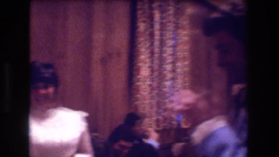 A woman in a white formal dress and a man in a light blue tuxedo jacket face each other inside a wood-paneled Boston interior in 1974.