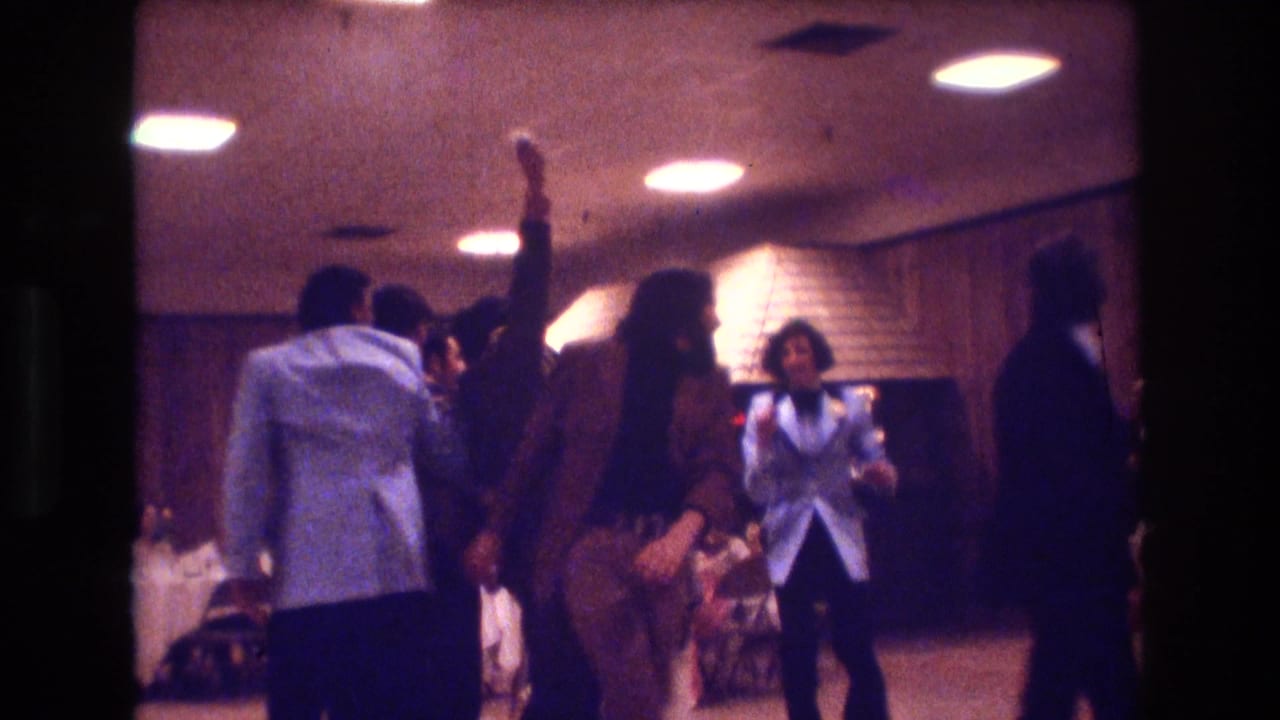 Young adults dancing and socializing under ceiling lights in a banquet-style room.