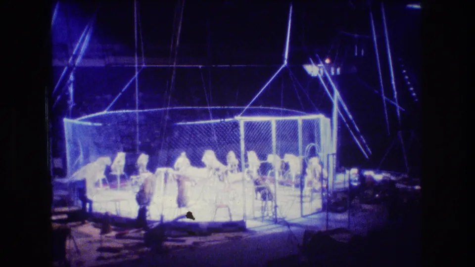 A heavily blue, overexposed 8mm frame shows the cage ring, small performer figures, and likely lions continuing the circus act in Boston metadata context.