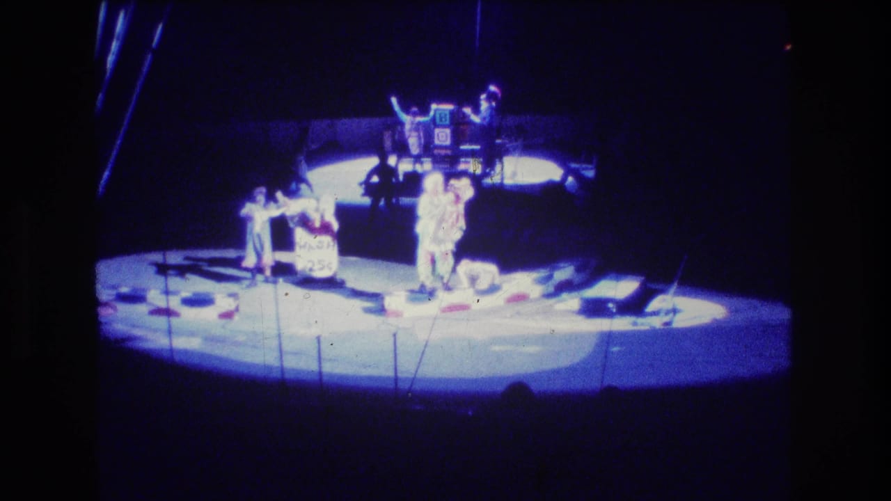 Circus performers continue a stage routine under strong blue lighting.