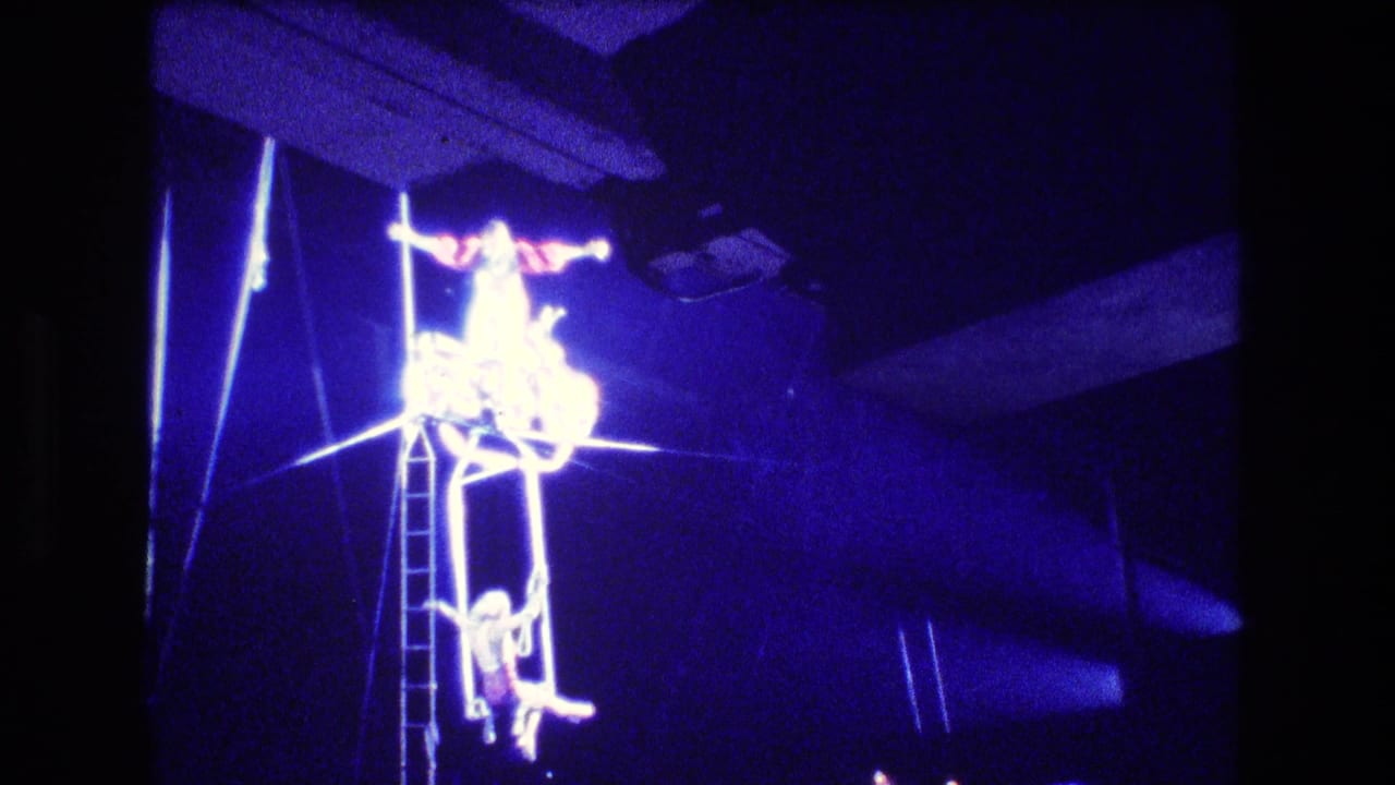 Boston 1974 8mm circus footage showing an acrobat on elevated rigging above a ladder in intense blue stage lighting.