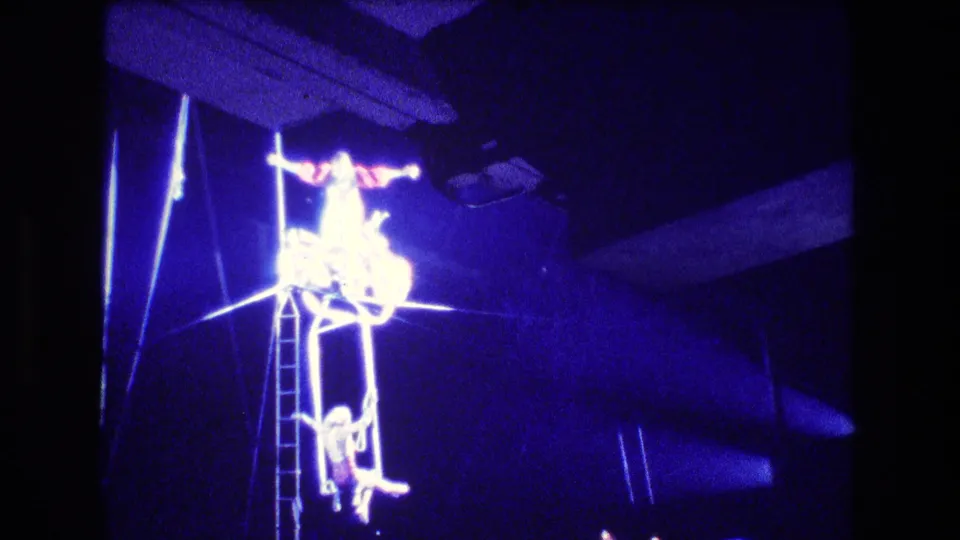 Boston 1974 8mm circus footage showing an acrobat on elevated rigging above a ladder in intense blue stage lighting.