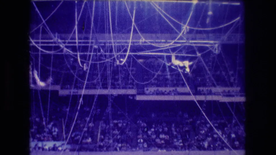 1974 Boston 8mm frame showing a distant acrobat amid hanging ropes and trapeze equipment, with the audience visible in the lower stands.
