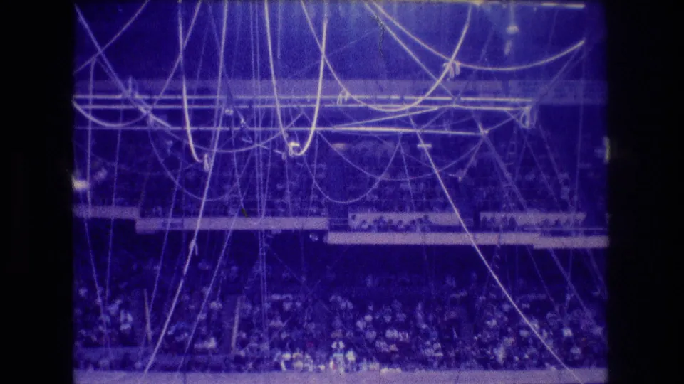 1974 Boston 8mm frame of the circus rigging network over a packed arena, with performers difficult to distinguish in the blue-purple home-movie exposure.