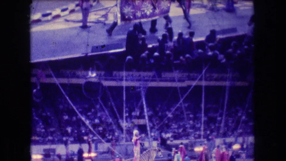 A grainy 8mm view shows the elephant act partly at the edge of the frame, with spectators in the foreground and circus rigging visible across the arena.