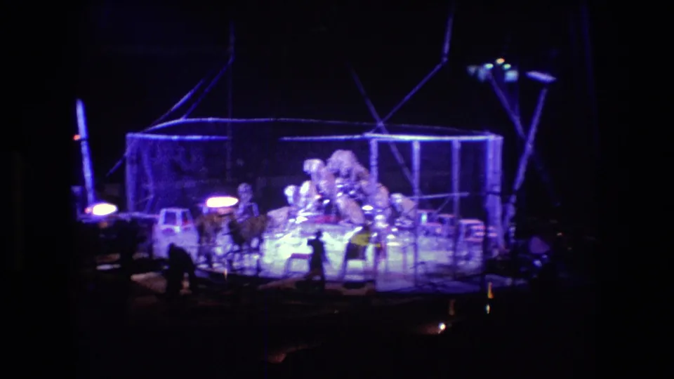 Final 1974 Boston circus frame with performers clustered near a bright metal rig or enclosure on a darkened arena floor, recorded with strong Super 8 color shift.