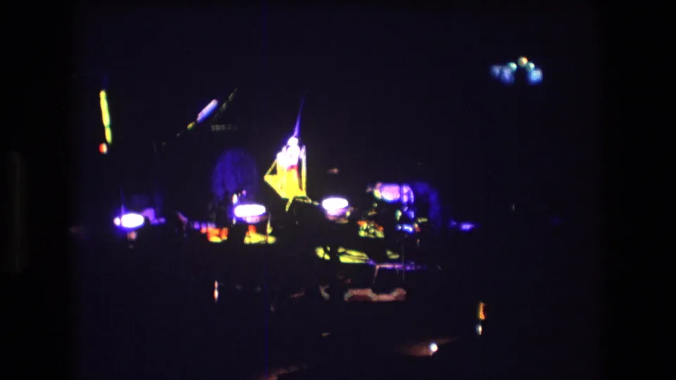 Boston 1974 8mm frame showing a distant indoor circus stage under purple light with bright spotlights and indistinct performers or equipment.
