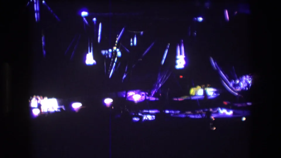 Boston 1974 8mm frame showing a dark circus performance area with hanging apparatus, scattered spotlights, and blurred illuminated set pieces.