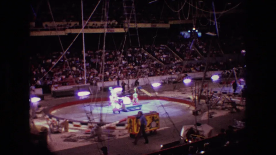 1974 Boston arena circus scene with a crowded audience, illuminated ring, visible rigging, and performers moving around the ring area.