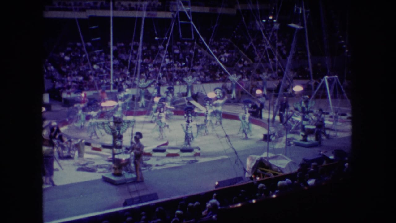 1974 Boston 8mm home-movie frame showing a wide view of circus dancers and acrobats performing under rigging before a large arena audience.