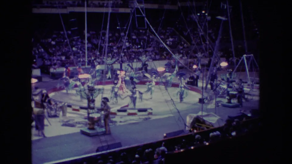 Wide 1974 Boston home-movie view of a circus act with performers on the arena floor, visible rigging overhead, and rows of spectators behind them.