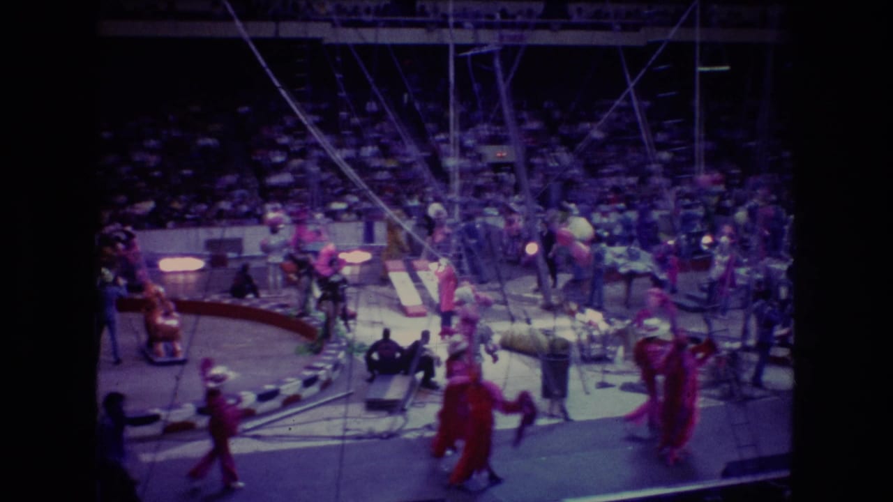 Costumed circus performers and ring equipment are visible in front of a seated arena audience.