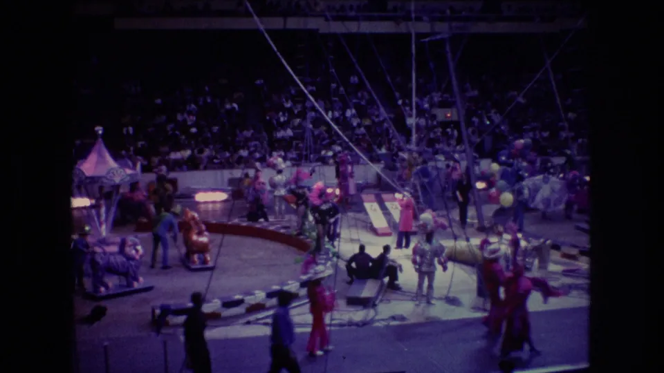 1974 Boston 8mm frame gives a wider spectator view of the circus ring, with performers, rigging, props, ring barriers, and a crowded seating section visible.