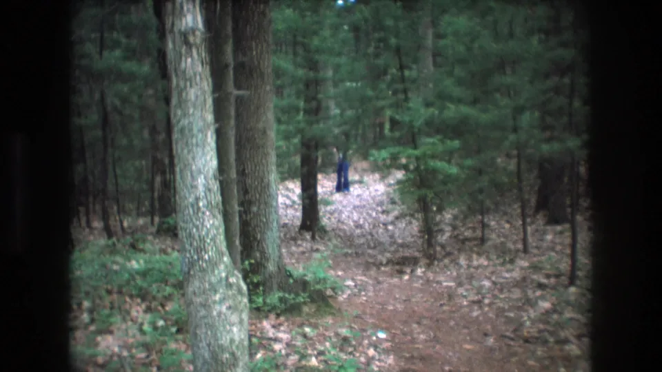 1975 Baxter, Maine 8mm frame showing a dirt path receding through trees, with a distant person in blue near the center background.