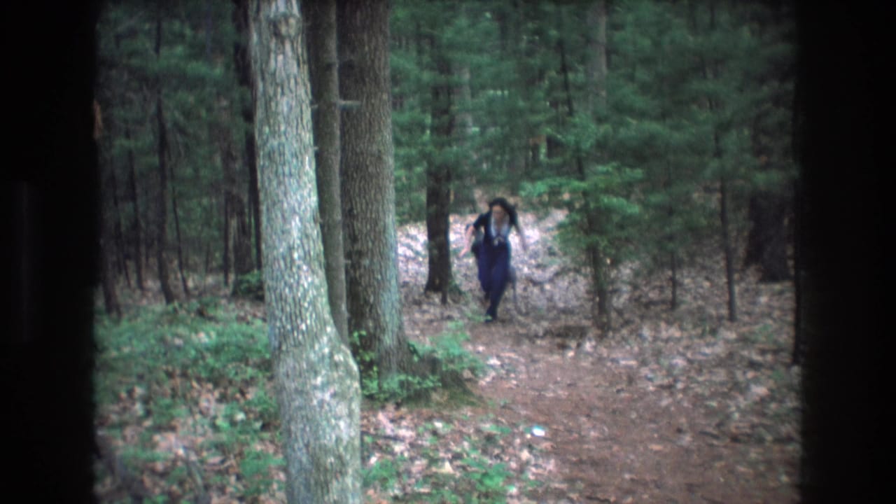 Young woman runs closer along a wooded path with a dog nearby.