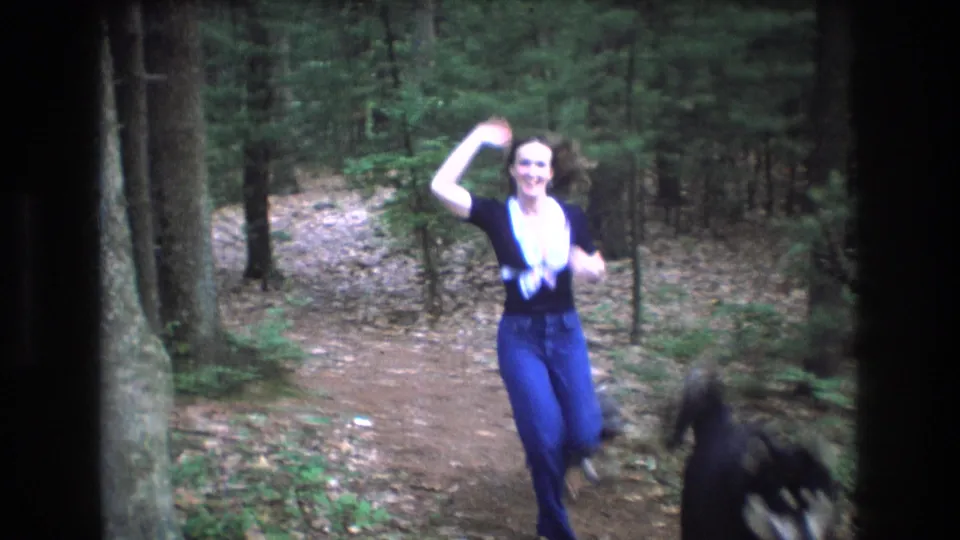 Near the end of the 1975 Baxter, Maine home-movie shot, the young woman smiles and waves close to the camera while a small dog passes through the foreground.