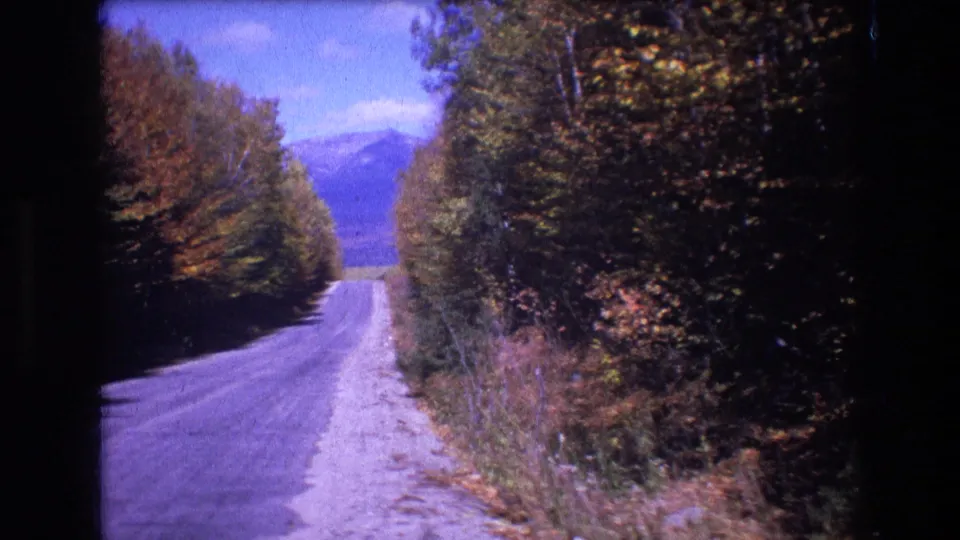 The road continues through wooded Baxter, Maine scenery, with autumn foliage, roadside brush, and hazy mountains visible beyond the tree corridor.