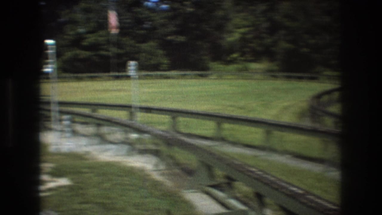 Green wooden track curves through a grassy fenced area with trees behind it.