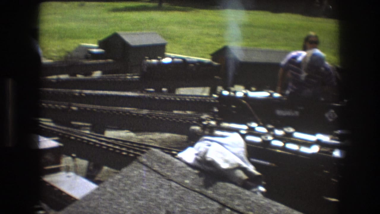 Black miniature steam locomotive beside tracks and small buildings.