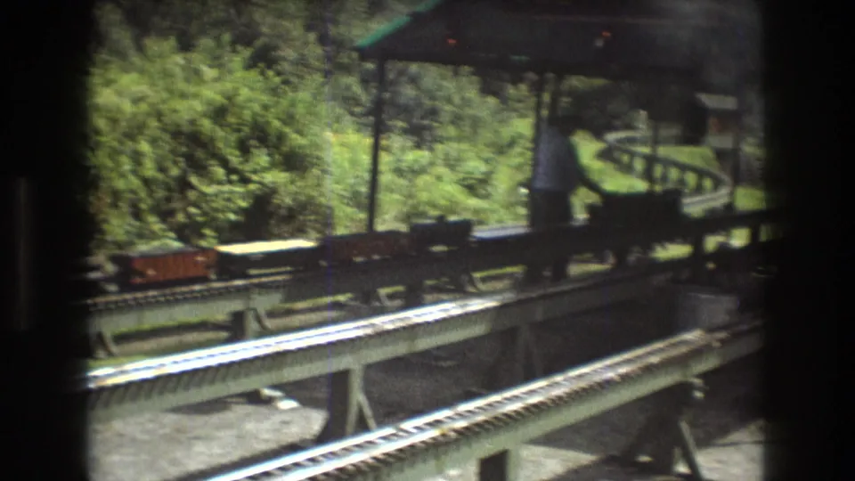 The final 1975 Baxter, Maine frame shows raised miniature railway tracks, a small train car, a covered platform, and surrounding green vegetation in soft 8mm color.
