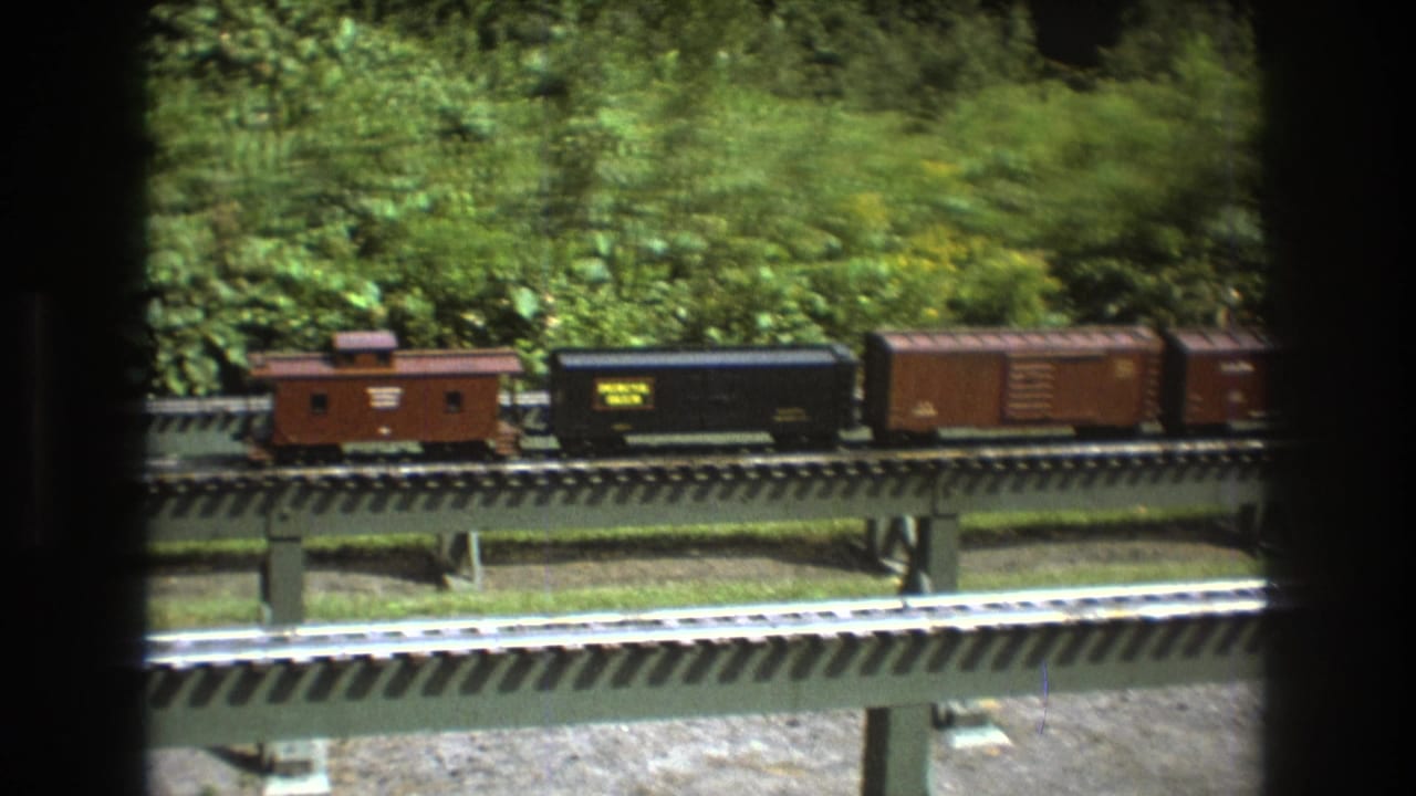 A caboose, black freight car, and brown boxcar on a model railway bridge.