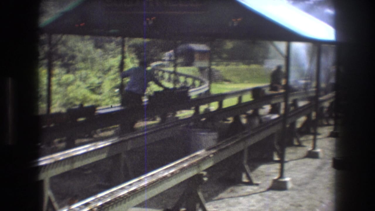 Worker leans over a small train display with smoke near the covered track area.