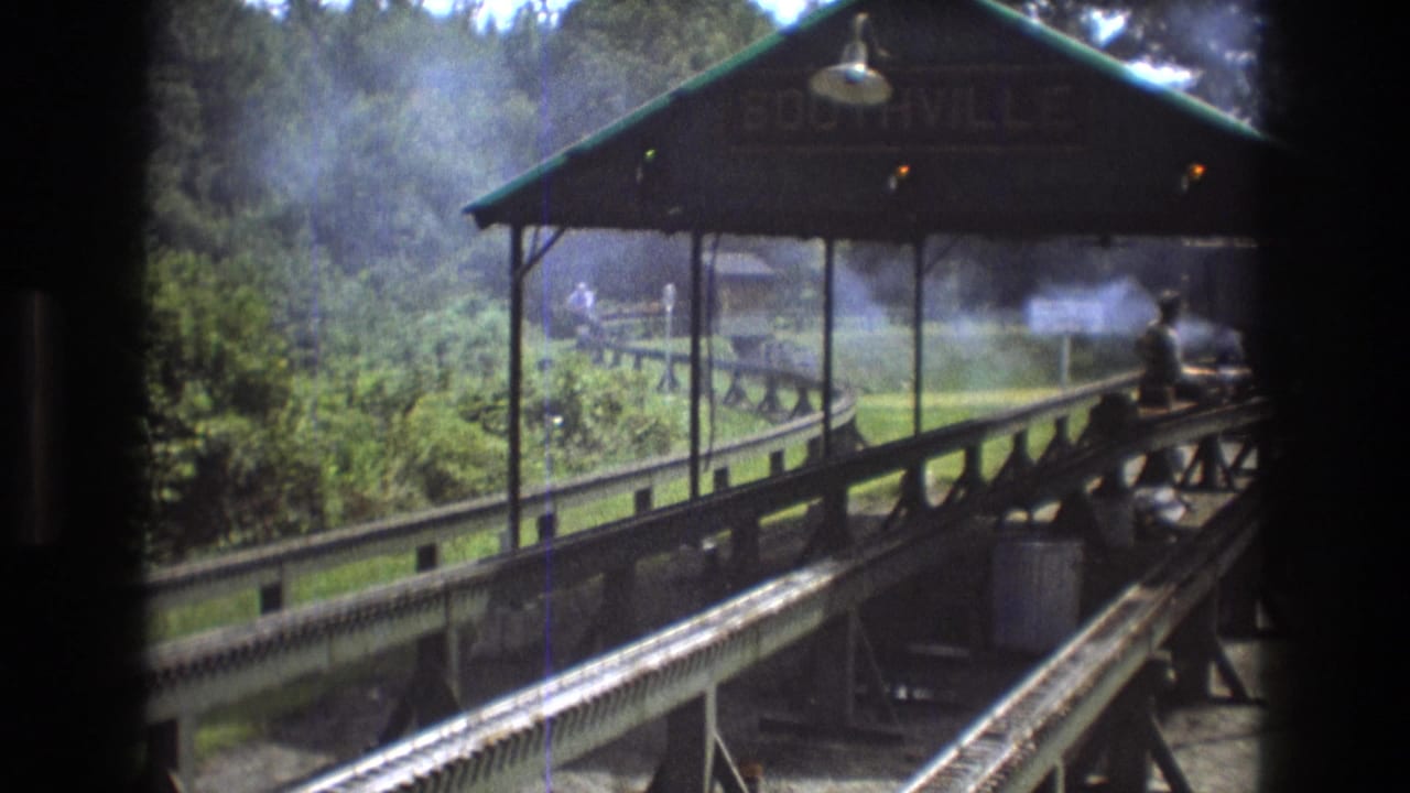 Miniature railway tracks lead toward a covered station with a Southville sign and smoke nearby.