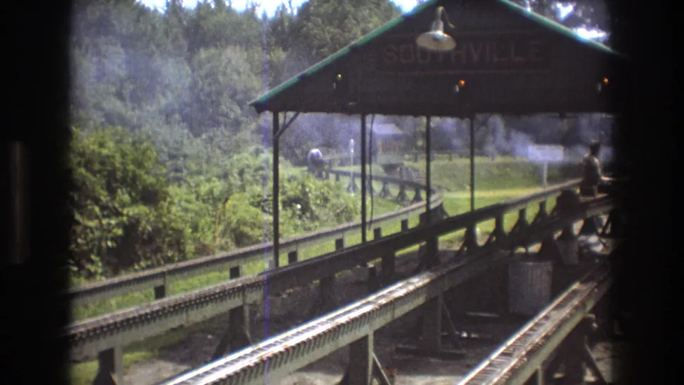 The Baxter, Maine miniature railway scene shows the Southville station shelter, rails, smoke or steam, and a rider near the right side of the frame.