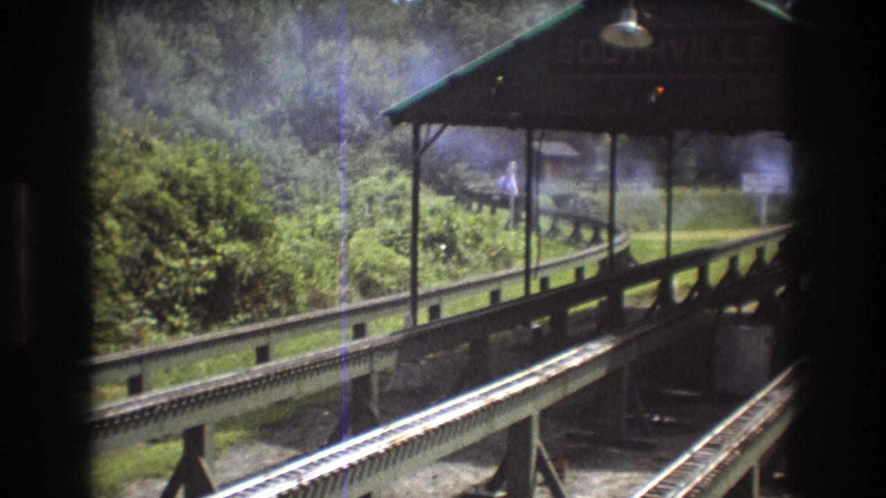 Rail tracks lead toward a platform canopy with smoke drifting behind it.