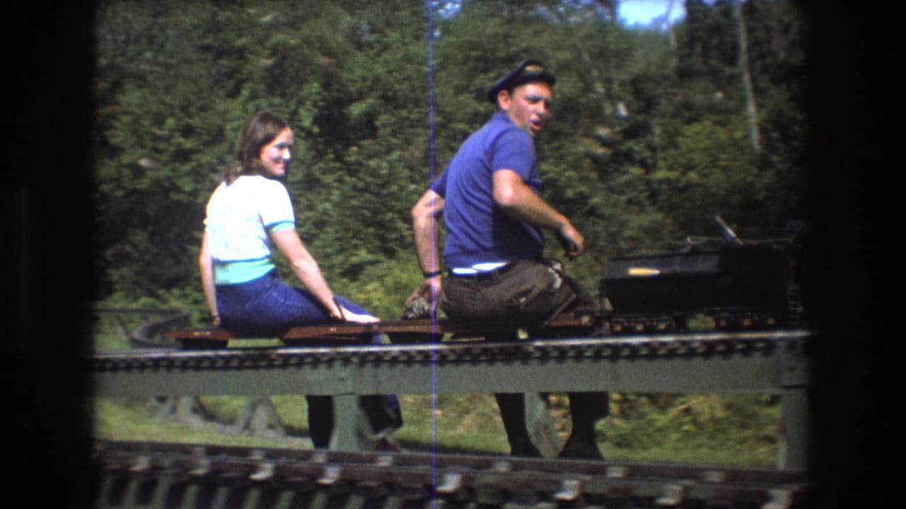 Young woman smiles toward the camera as a young man sits beside her on a miniature train.
