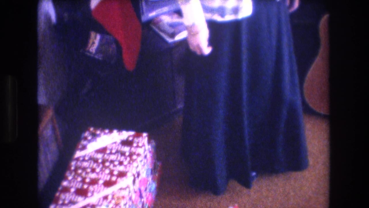 Woman near a long blue skirt or dress and a patterned box-like object in a living room.