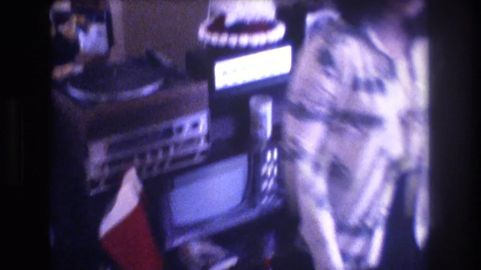 Close handheld frame of living room electronics, a red Christmas stocking, and part of the woman’s patterned outfit in Baxter, Maine, 1975 home-movie footage.
