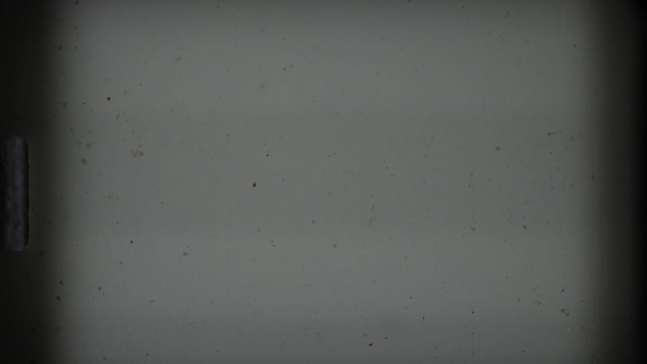 An underexposed 8mm frame from the Boston 1975 home-movie clip shows mostly a pale wall or leader-like area with film edge marks and little discernible kitchen detail.