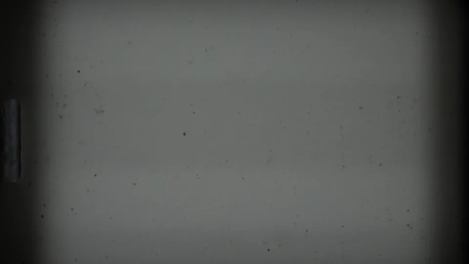 An underexposed 8mm frame from the Boston 1975 home-movie clip shows mostly a pale wall or leader-like area with film edge marks and little discernible kitchen detail.