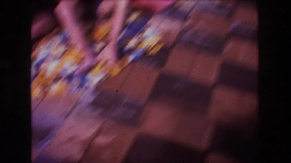 The camera swings or shakes, creating a blurred view of the colorful blanket, legs, patio paving, and strong shadows.
