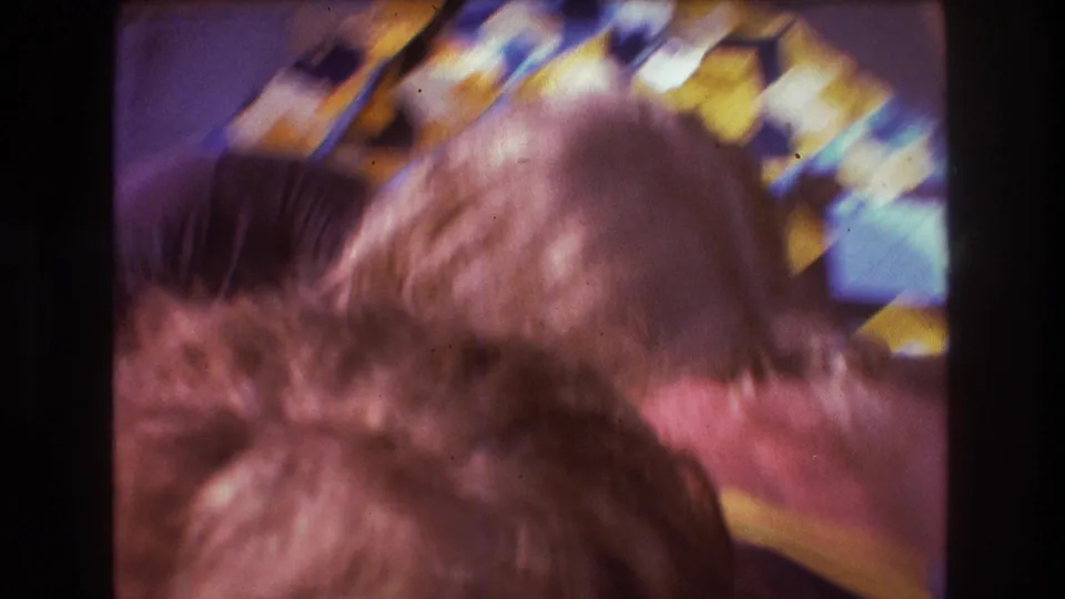 Blurred 1975 Boston 8mm frame showing two people in close movement on colorful blankets during a casual outdoor hangout.