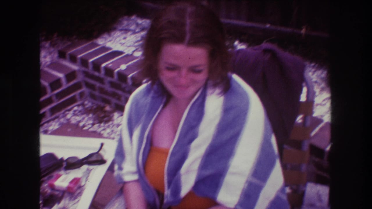 Woman in a striped towel looks downward while seated beside sunglasses on an outdoor table.