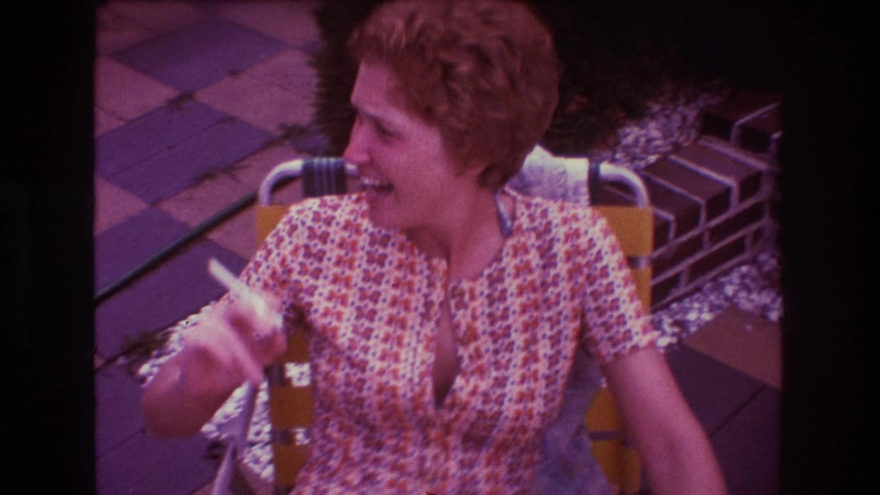 Woman seated outdoors turns to the side while smiling and holding a cigarette.