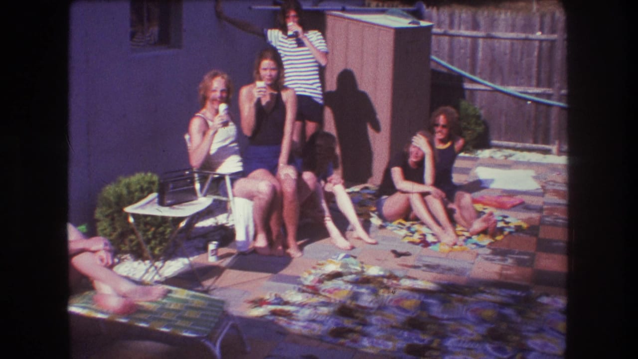 Group of friends sit and stand around patio chairs and blankets in a backyard.