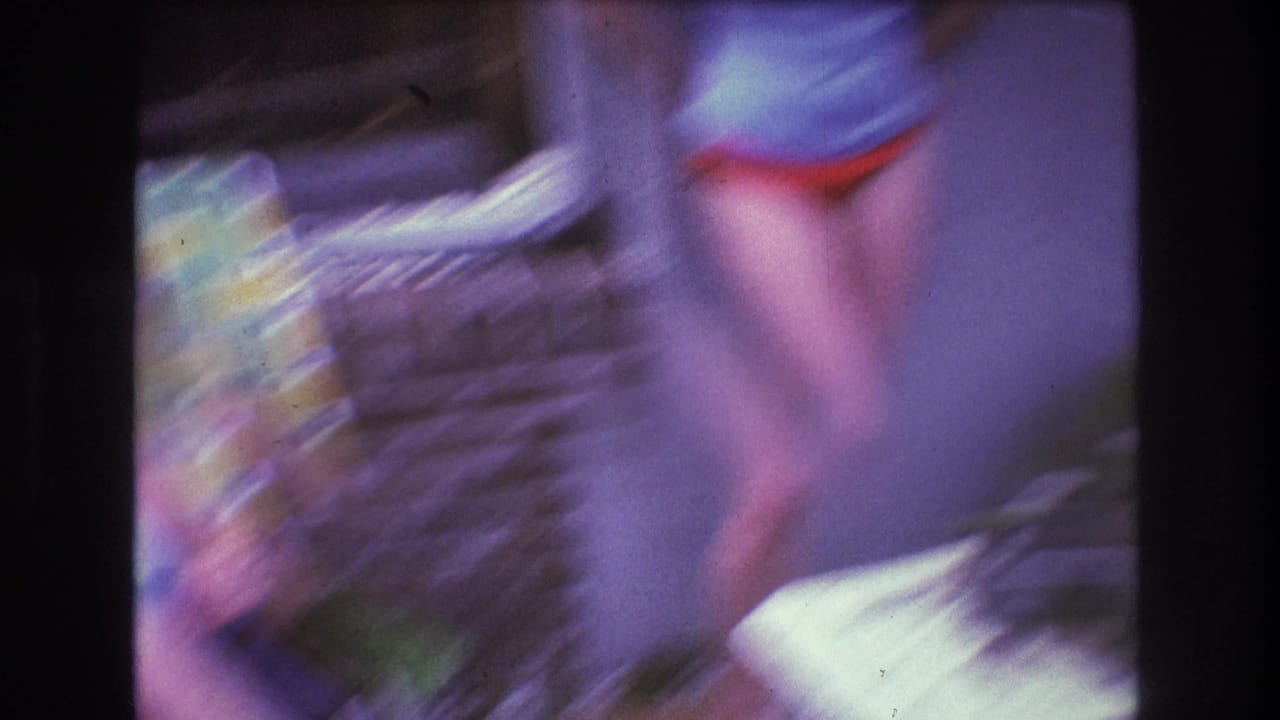 A heavily blurred handheld 8mm frame shows a person moving close to the camera near the patterned lawn chair during the backyard gathering.