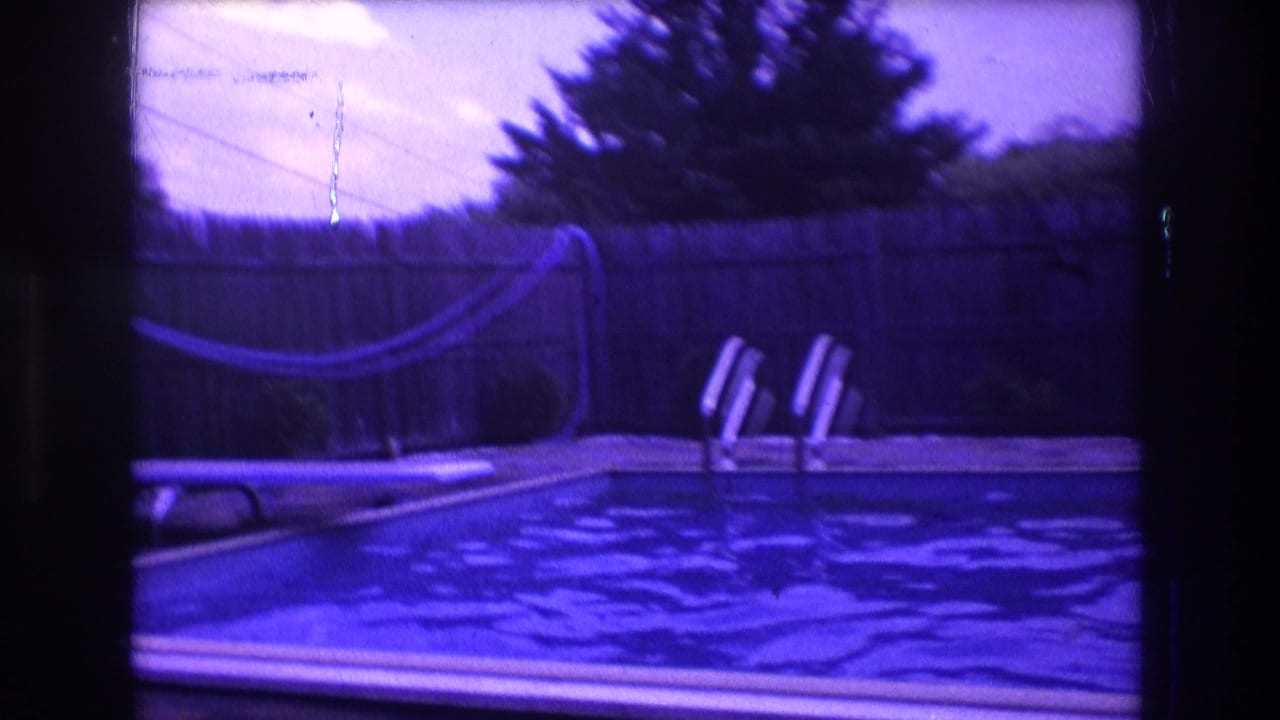 1975 Boston backyard pool view with rippling water, two lounge chairs, a wooden fence, trees, and a hose visible through aged purple-blue 8mm color shift.