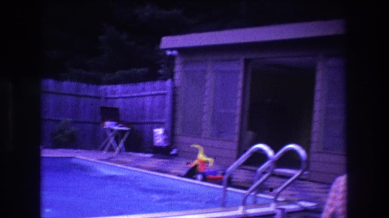 1975 Boston backyard poolside frame with metal ladder rails in the foreground, a wood fence, small shed, folding chair, and toy near the pool edge.