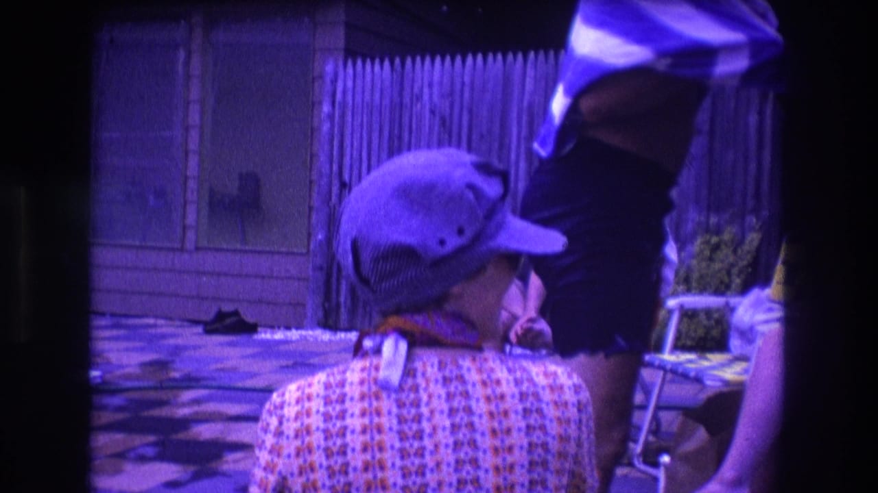 Person in cap seen from behind near a standing man with a striped towel and a seated figure at the edge of frame.