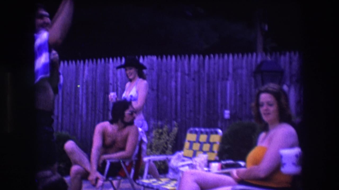 1975 Boston 8mm home-movie frame showing adults at a nighttime backyard pool party, with swimwear, drinks, folding chairs, and a wooden fence visible.