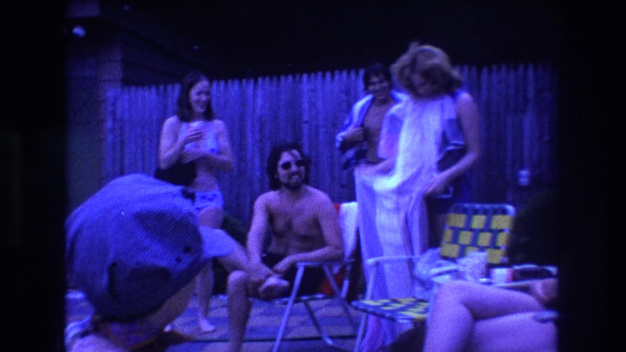 Several young adults stand and sit near patio chairs in a fenced yard.