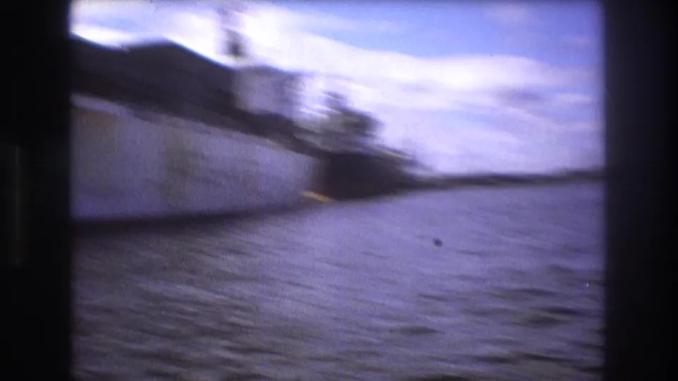A motion-blurred 8mm frame shows the side of a large ship over harbor water, with the camera moving quickly along the waterfront.