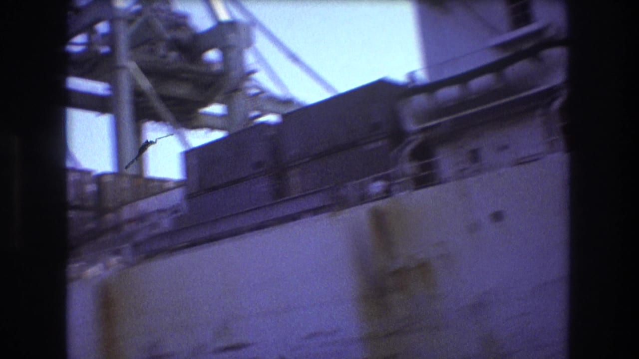 Handheld 8mm frame from the Boston dockside view, showing blurred ship railings, deck structures, a pale hull section, and overhead industrial equipment.