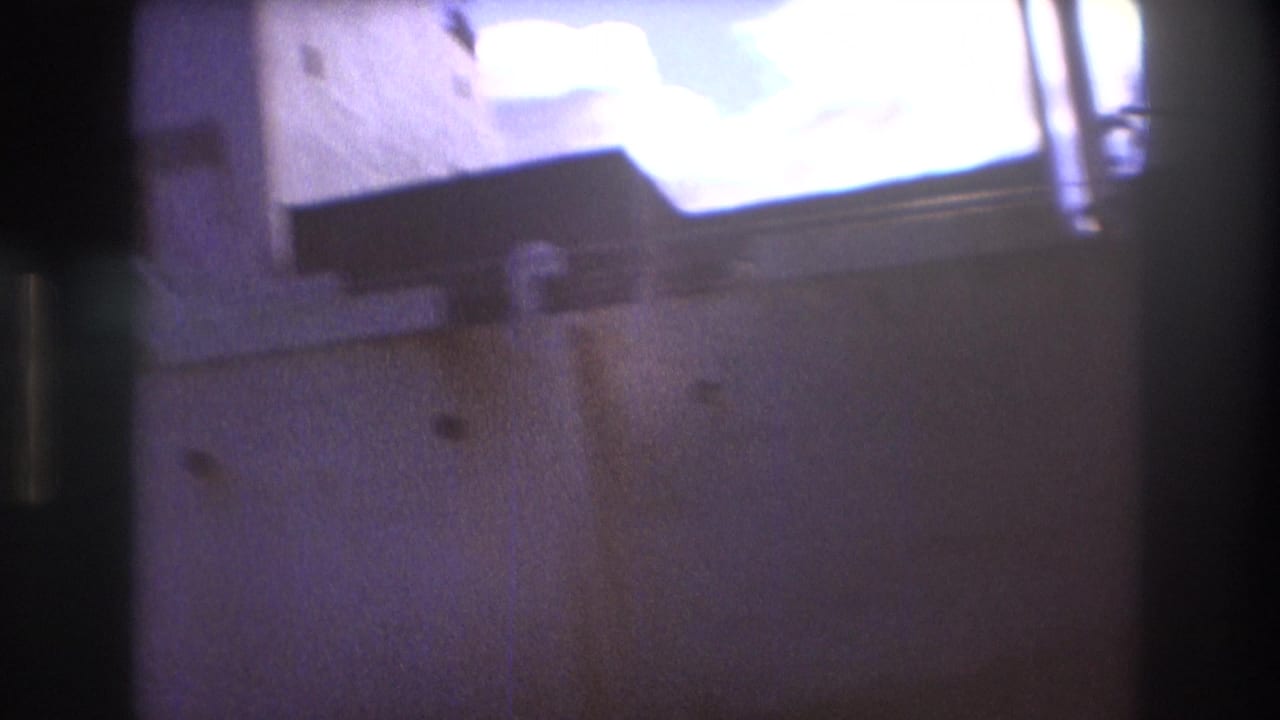 Soft final 8mm frame from the 1975 Boston harbor clip, with the freight ship hull and dockside structure blurred by close handheld movement and bright exposure.