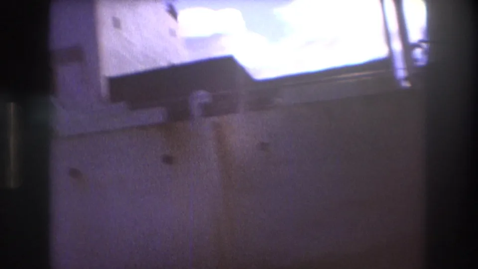 Soft final 8mm frame from the 1975 Boston harbor clip, with the freight ship hull and dockside structure blurred by close handheld movement and bright exposure.